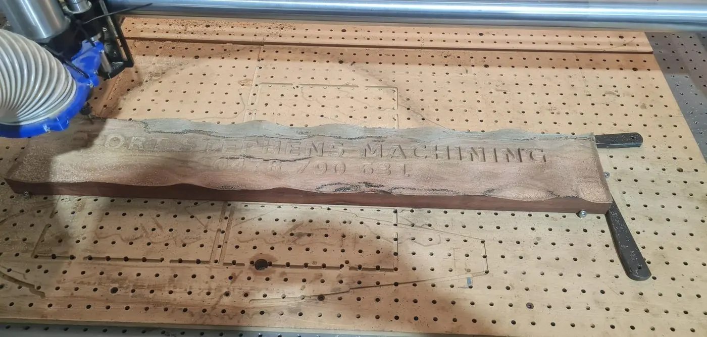 A hardwood board carved with a wave background and raised lettering, on the router bed
